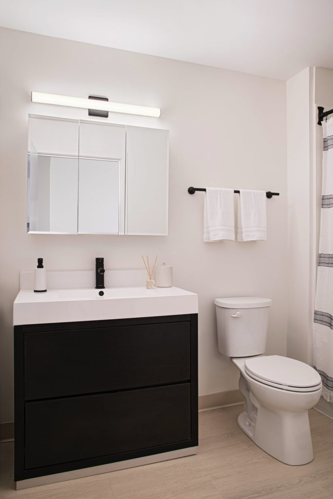 A modern bathroom design with mirrored cabinet, black vanity, and white sink