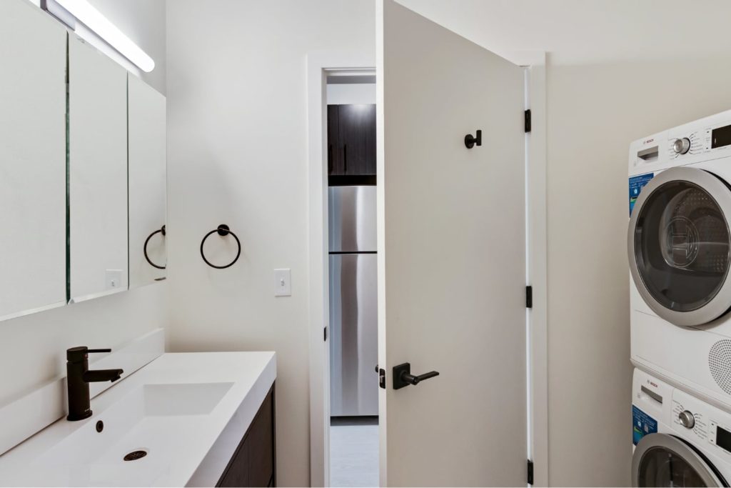 A modern bathroom with black fixtures and stacked laundry unit.
