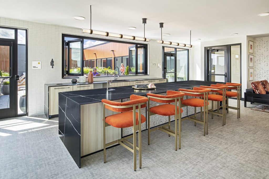 A large kitchenette with a black stone waterfall island and orange velvet barstools.