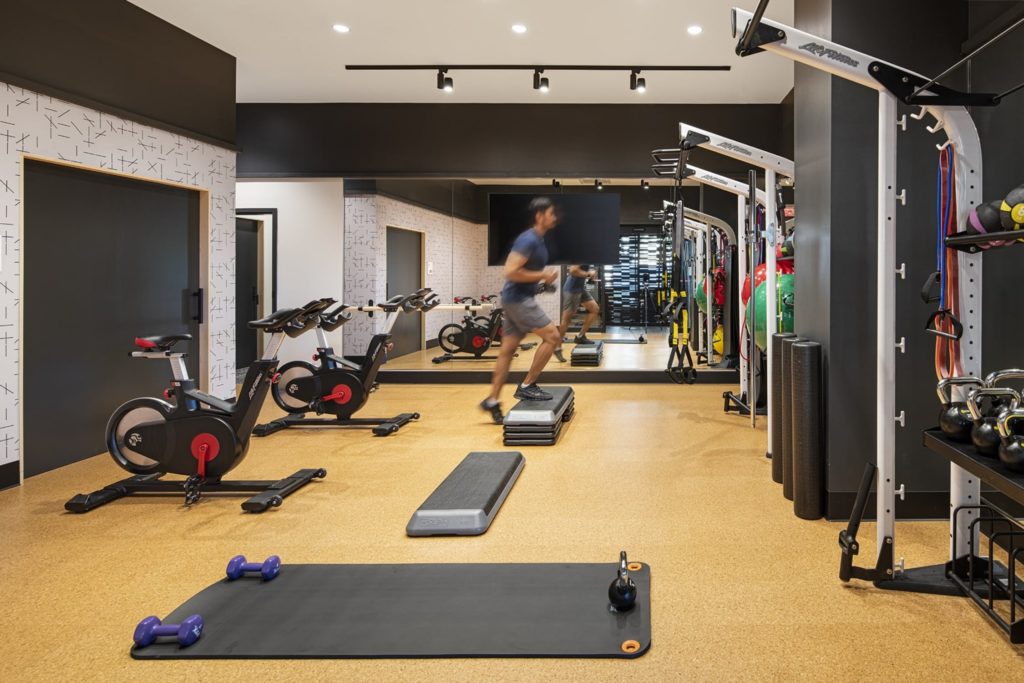 A man works out in a studio, including stationary bikes, mats, and circuit training equipment.