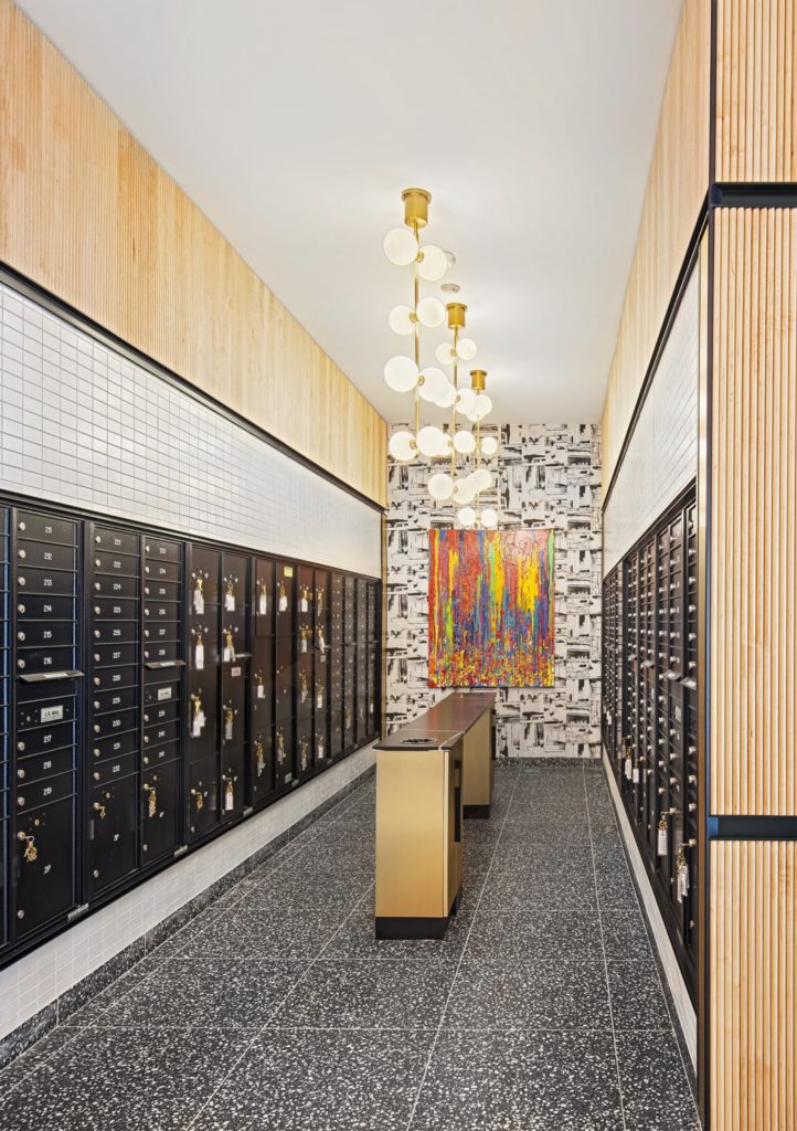 A hallwall full of small mailbox lockers. Decorative wallpaper and wood accents highlight tile walls.