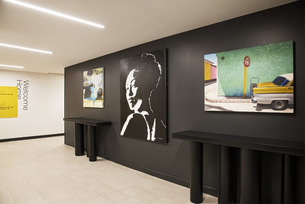 Three paintings hang across from a set of elevators. The walls are painted black to highlight the paintings.