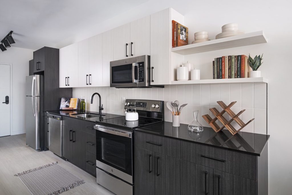 The kitchen in a Woodward West apartment, with gray-black lower cabinets, white uppers, a tile backsplash, and black fixtures.